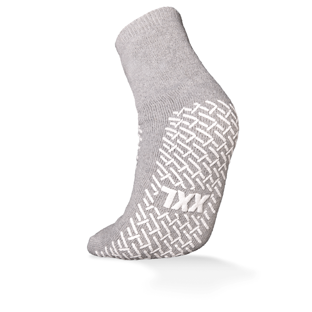 Egyetlen szürke ECO-PLUS csúszásgátló eldobható zokni látható az AMPri Handelsgesellschaft mbH-tól, fehér csúszásgátló fogantyúval és "TXX" felirattal a talpon. Mindkét oldalon bevonva, ideális orvosi területekre; a háttér egyszerűen fehér.