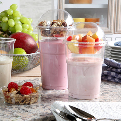 Két joghurtparfé műanyag poharakban, mindegyik lezárva egy Starpak 50 Dom-fedél „Hurricane” PET kerek átlátszó Ø 9,5 cm-es fedéllel, egy konyhapulton áll – az egyik müzlivel és dióval, a másik gyümölcsökkel. A háttérben friss bogyók és egymásra rakott tányérok láthatók.