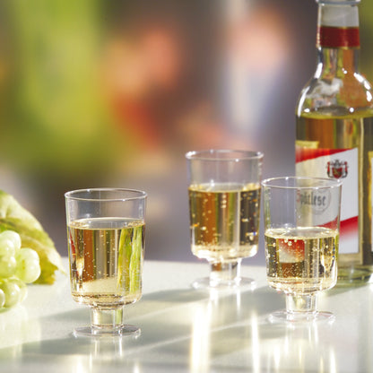 Három Starpak fehérboros pohár (PS, 0,1l, üvegtiszta) van megtöltve, és egy fehérboros palack, valamint zöld szőlő mellett állnak fehér felületen homályos háttér előtt.