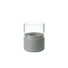 Der Kerzenhalter Glas Neat 70 x 61 mm von Duni GmbH zeichnet sich durch eine klare Glasplatte und einen hellgrauen Betonsockel mit glatten Oberflächen und klaren Linien aus, wodurch ein minimalistisches, modernes Wohnaccessoire entsteht.