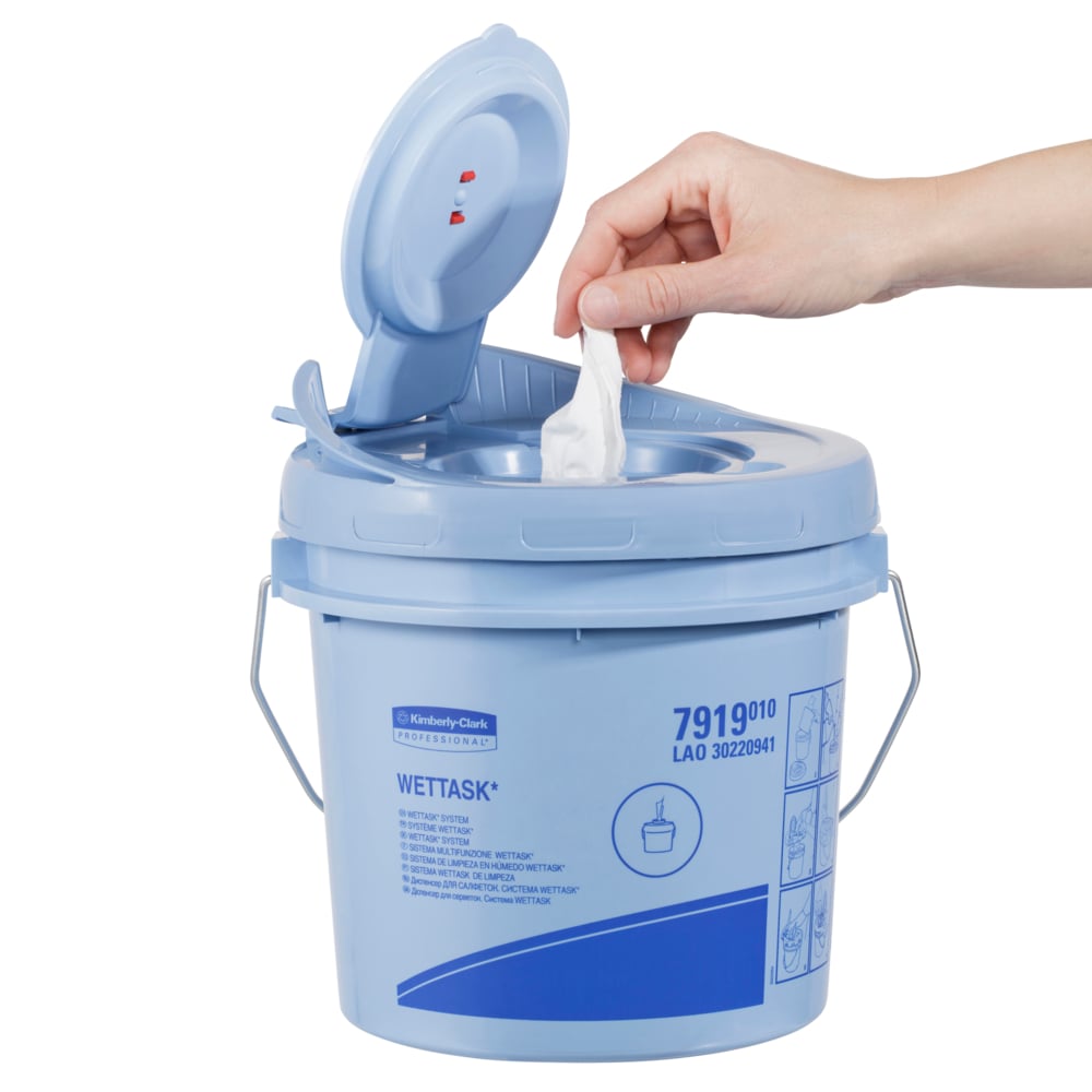 Eine Hand zieht ein WypAll® Wettask™ PowerClean-Tuch aus einem hellblauen Behälter der Kimberly-Clark GmbH mit Flip-Top-Deckel. Die Schachtel enthält 6 Rollen mit je 60 Blatt und ist auf der Seite mit Produktinformationen und Abbildungen bedruckt.