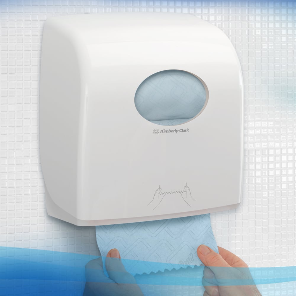 Egy fehér adagoló a Kimberly-Clark GmbH-tól Scott® Essential™ Slimroll™ kéztörlőkhöz (190,00 m x 19,80 cm) falra szerelve, egy kéz, amely egy kék törlőt húz ki, látható a kerek ablakban környezetbarát kézszárításhoz.