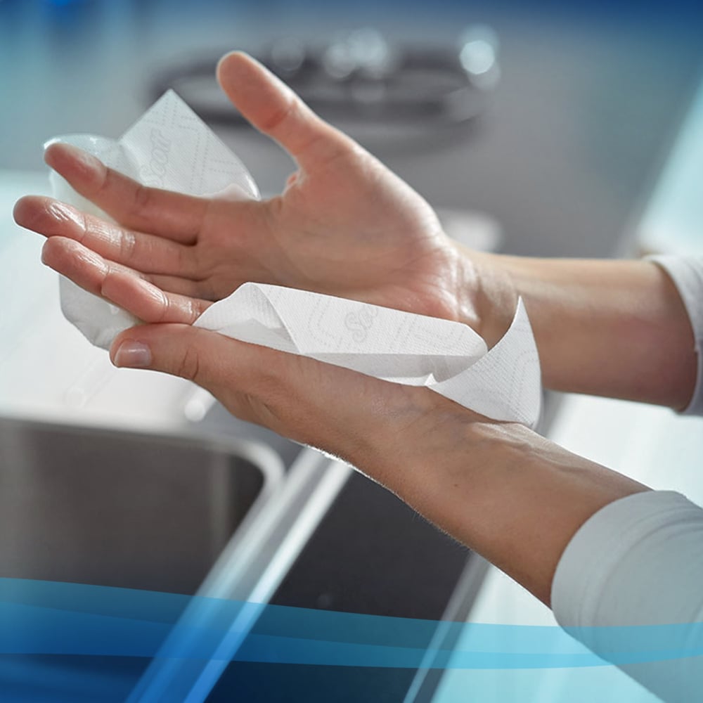 Egy személy szárítja a kezét Scott® Essential™ Slimroll™ kéztörlőkkel (190,00 m x 19,80 cm) a Kimberly-Clark GmbH-tól, környezetbarát kézszárítást használva egy modern konyhában a mosogató közelében.