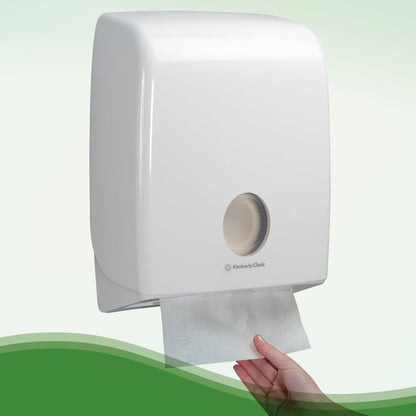 Egy kéz húz ki egy Hostess™ NATURA™ fehér kéztörlőt a Kimberly-Clark GmbH-tól egy falra szerelt adagolóból, fehér műanyag fedéllel és betekintő ablakkal - ideális nyilvános mosdók számára. 20 klip x 84 lap/doboz.