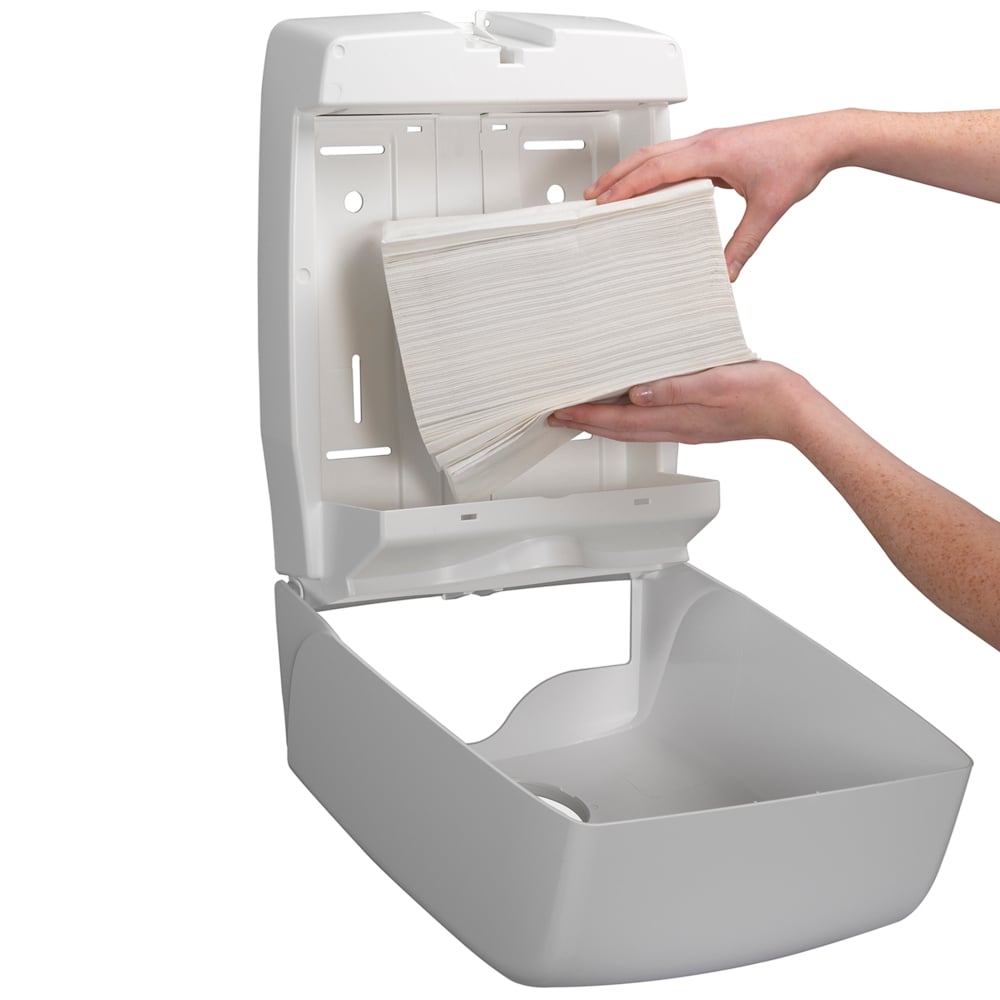 Egy személy egy falra szerelt adagolót tölt fel Kleenex® Ultra™ hajtogatott kéztörlőkkel, Fehér (15 csipesz x 96 lap) a Kimberly-Clark GmbH-tól, biztosítva a higiénikus kézszárítást, mivel a nyitott adagoló egyszerű utántöltést tesz lehetővé.