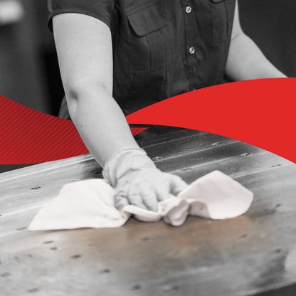 Egy rövid ujjú inges személy töröl le egy nagy fémfelületet egy kendővel, valószínűleg egy Kimberly-Clark GmbH WypAll® X60 General Clean a BRAG™ Boxból (41,80 cm x 28,30 cm); a kép főként fekete-fehér, közepén egy élénk piros átlóval.