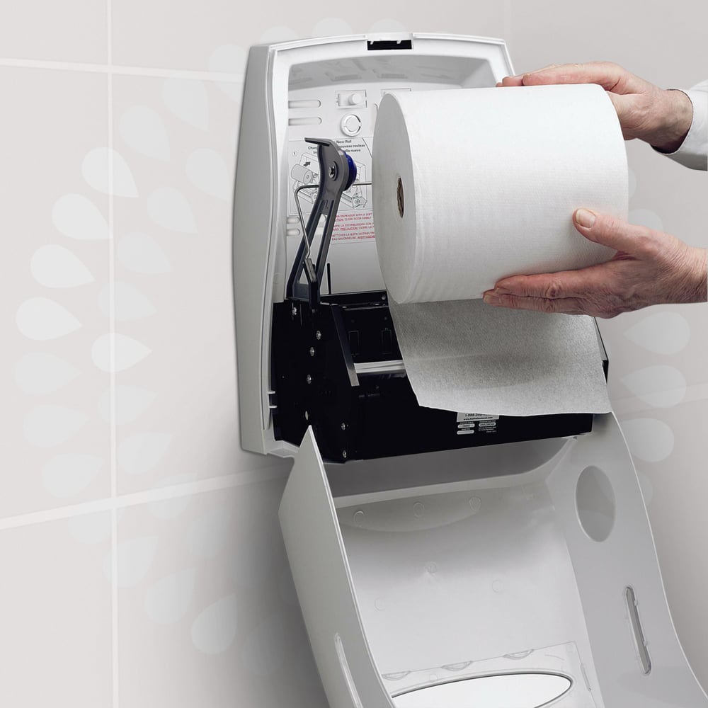 Egy személy egy Kleenex® Ultra™ kéztörlő - tekercset a Kimberly-Clark GmbH-tól egy fehér, nyitott falra szerelhető adagolóba helyez el egy mosdóban, hogy biztosítsa a higiénikus kézszárítást. Az adagoló fedelén egy útmutató van nyomtatva.