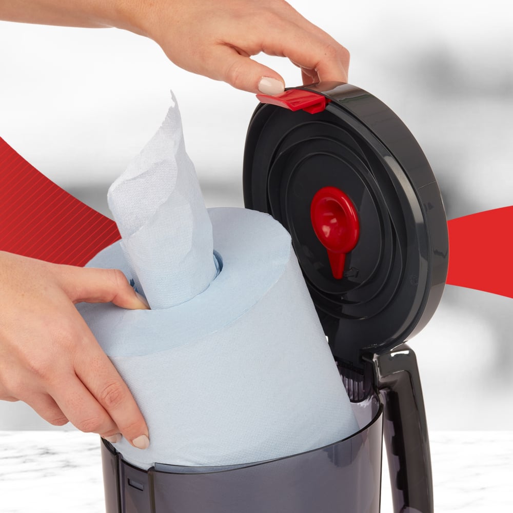 Egy felhasználó egy nagy kék tekercset helyez a nyitott WypAll® Reach™ Centrefeed adagolóba (fekete) a Kimberly-Clark GmbH-tól, amely a piros kioldó mechanizmust mutatja - tökéletes professzionális használatra.