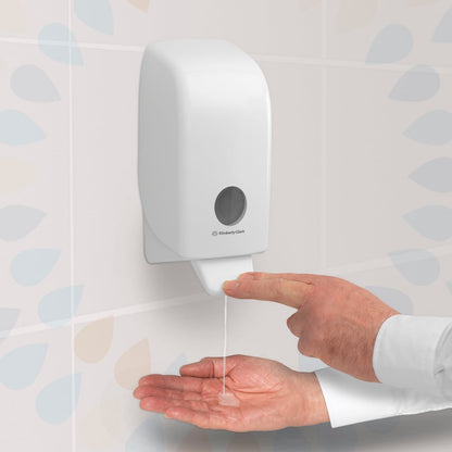 Egy személy megnyom egy átlátszó Kleenex® Extra Gel kézfertőtlenítő adagolót a Kimberly-Clark GmbH-tól, amely egy csempézett falra van szerelve, és a kézfertőtlenítő gélt egy 1 literes kazettából a nyitott tenyérére adagolja.