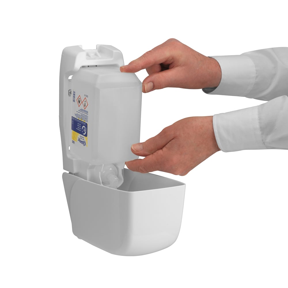 Egy személy feltölt egy falra szerelt Kimberly-Clark GmbH Kleenex® Extra Gel kézfertőtlenítő adagolót, miközben mindkét kezével behelyez egy új átlátszó 1 literes kazettát; a nyitott előlapon csak a kezei és alkarjai láthatók.