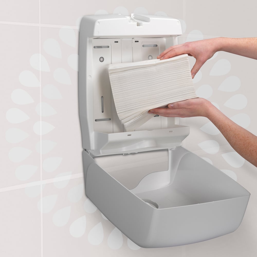 Egy személy egy halom Kimberly-Clark GmbH Kleenex® Ultra™ MultiFold kéztörlőt (fehér, kicsi, 18 csomag x 150 lap) tölt be egy falra szerelt papírtörlő adagolóba egy WC-ben.