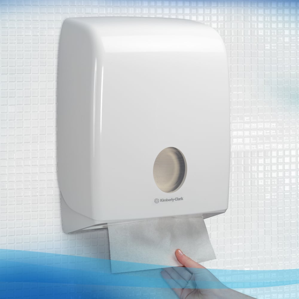 Eine Hand zieht ein Scott® Control™ Interfold Handtuch aus einem weißen Kimberly-Clark Spender in einen gefliesten Waschraum und sorgt so für hygienische Händetrocknung.
