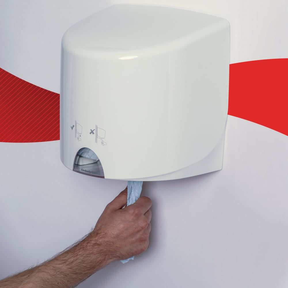 Egy kéz húz ki egy kék WypAll® L10 papírtörlőt élelmiszerhez és higiéniához a Kimberly-Clark GmbH-tól egy fehér falra szerelt adagolóból egy fehér fal előtt, piros hullámcsíkkal.