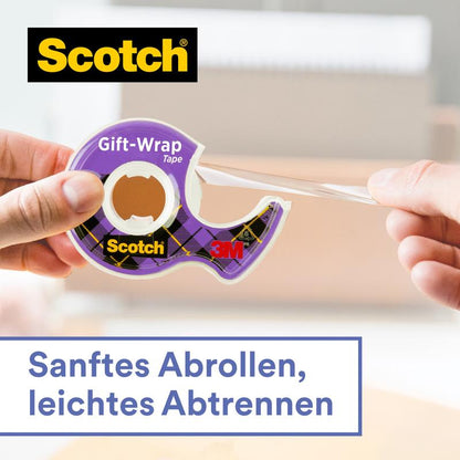 Egy kéz húzza le a tiszta Scotch® ajándék ragasztószalagot a kézi adagolóban, CAT 15 (19 mm x 15 m) a 3M Deutschland GmbH-tól. Szöveg: "Lágy letekerés, könnyű leválasztás." Homályos háttér irodai vagy lakótérrel.