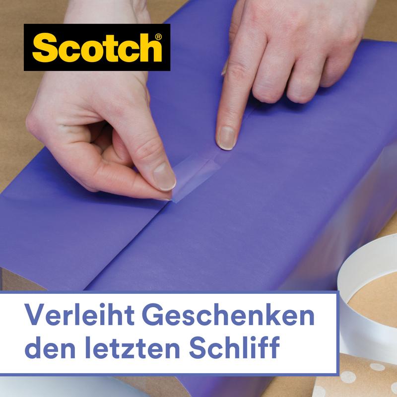 Egy személy kék csomagolópapírt zár le a Scotch® ajándék ragasztószalag kézi adagolóban, CAT 15 (19 mm x 15 m) a 3M Deutschland GmbH-tól. További ragasztószalag és az adagoló mellette fekszik. Német szöveg: "Végső simítást ad az ajándékoknak."
