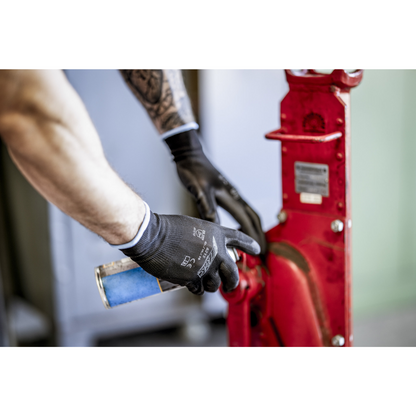 Egy személy NITRAS nejlonkesztyűben, fekete, PU-bevonatos az AS Arbeitsschutz GmbH-tól, tisztít vagy ken egy kék spray-dobozzal egy piros fémgépalkatrészt. Csak a karok és kezek láthatók.