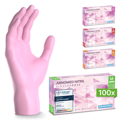 Ein rosafarbener ARNOMED NITRIL BLOSSOM ROSE Einmalhandschuh der ARNOWA GmbH ist geöffnet abgebildet, daneben stehen vier Kartons in den Größen XS, S, M und L. Die vordere Schachtel enthält 100 mittelgroße rosa Nitrilhandschuhe.
