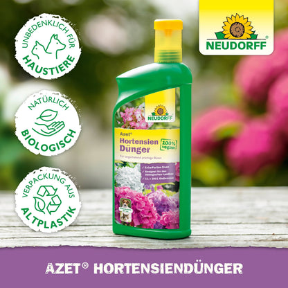 Egy zöld Neudorff Shop Azet HortensienDünger folyékony üveg virágképekkel a címkén, ábrázolva pet-safe, organikus trágya és bioplasztik szimbólumokkal. A háttér elmosódott virágokat mutat.