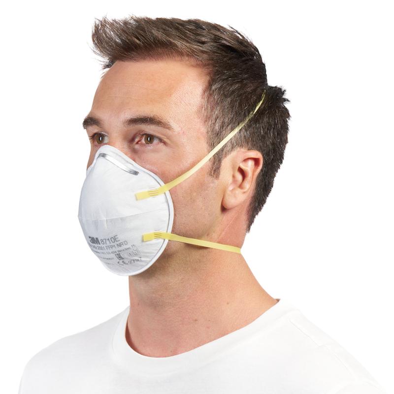 Egy rövid barna hajú férfi visel egy 3M™ 8710E részecskemaszkot, FFP1 (a 3M Deutschland GmbH-tól) sárga szalagokkal és szelep nélkül az orra és szája előtt, egyszerű fehér inggel párosítva fehér háttér előtt.