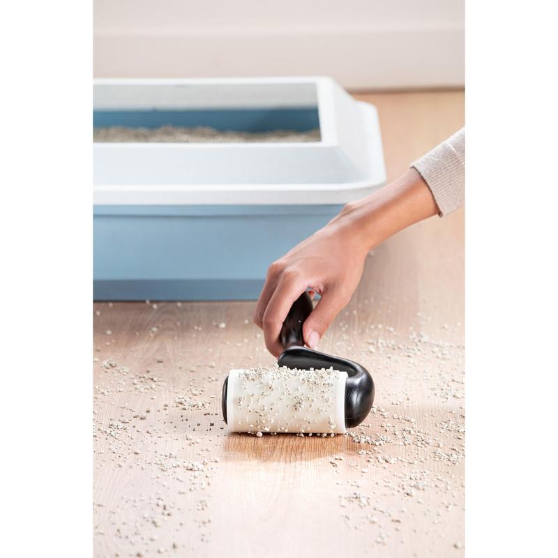 Egy kéz a 3M Deutschland GmbH Scotch-Brite™ Everyday Clean szöszeltávolító lapos felületekre (56 lap, 1/csomag) termékkel felszórt macskaalmot szed fel egy fapadlóról, a háttérben egy kék fedelű macskatoalett látható.