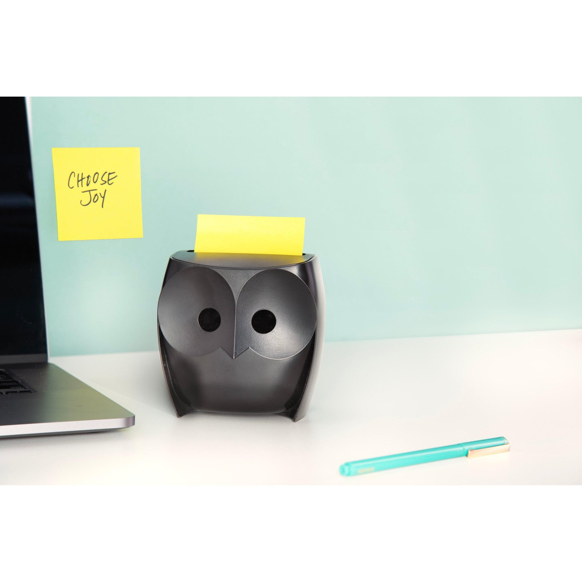 Ein Post-it® Z-Notes Dispenser im schwarzen Eulen-Design von 3M Deutschland GmbH hält gelbe Super Sticky Z-Notes (2 Blöcke, 45 Blatt/Block) auf einem weißen Schreibtisch mit einem Laptop, einem teal-goldenen Stift und einer "CHOOSE JOY"-Notiz vor einem hellblauen Hintergrund.