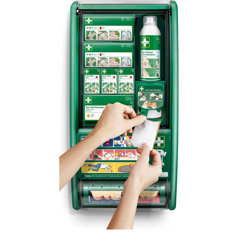 Egy személy egy kötést tart az Orkla Wound Care AB Cederroth elsősegély-állomása előtt, amely kötszerekkel, égési géllel, sóoldattal és kötszerekkel van felszerelve. Illusztrált utasítások láthatók a belső rekeszeken.