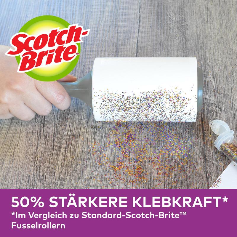 Egy kéz használja a Scotch-Brite™ Pet Extra Sticky* cserehenger állatszőrre (48 lap, 1/csomag) a 3M Deutschland GmbH-tól, hogy eltávolítsa a kiömlött csillámot a fáról. Egy nyitott csillámtartó van a közelben. "50%-kal erősebb tapadóerő" az alul látható standard hengerekkel összehasonlítva.