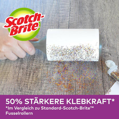 Egy kéz használja a Scotch-Brite™ Pet Extra Sticky* cserehenger állatszőrre (48 lap, 1/csomag) a 3M Deutschland GmbH-tól, hogy eltávolítsa a kiömlött csillámot a fáról. Egy nyitott csillámtartó van a közelben. "50%-kal erősebb tapadóerő" az alul látható standard hengerekkel összehasonlítva.