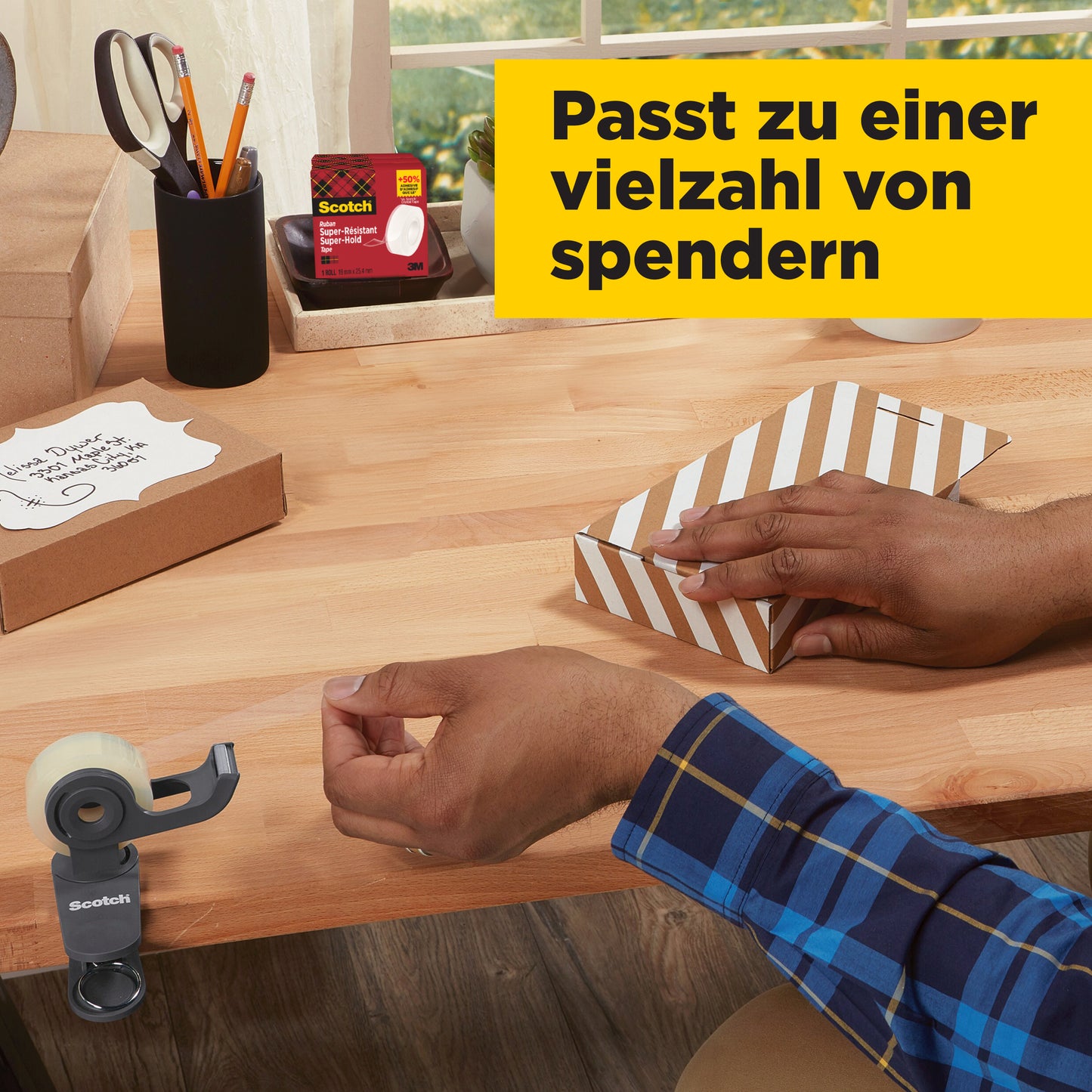 Eine Person in einem blau karierten Hemd klebt eine gestreifte Schachtel mit Scotch® Super-Hold Secure Tape, 1 Rolle, 19 mm x 25,4 m von 3M Deutschland GmbH auf einem hölzernen Schreibtisch mit Büromaterial und Geschenken; deutscher Text ist in einem gelben Kasten dargestellt.