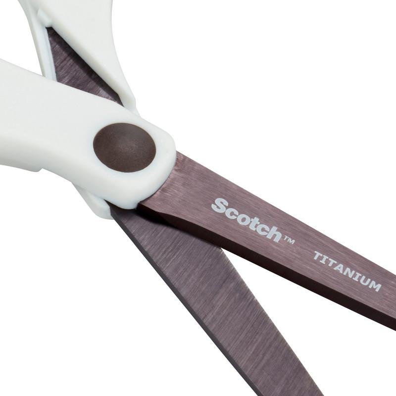 Közelkép egy pár 3M Deutschland GmbH Scotch™ titánium ollóról (20 cm) fehér fogantyúkkal és titánium pengékkel. Az egyik pengén "Scotch" és "Titanium" fehérrel van nyomtatva.