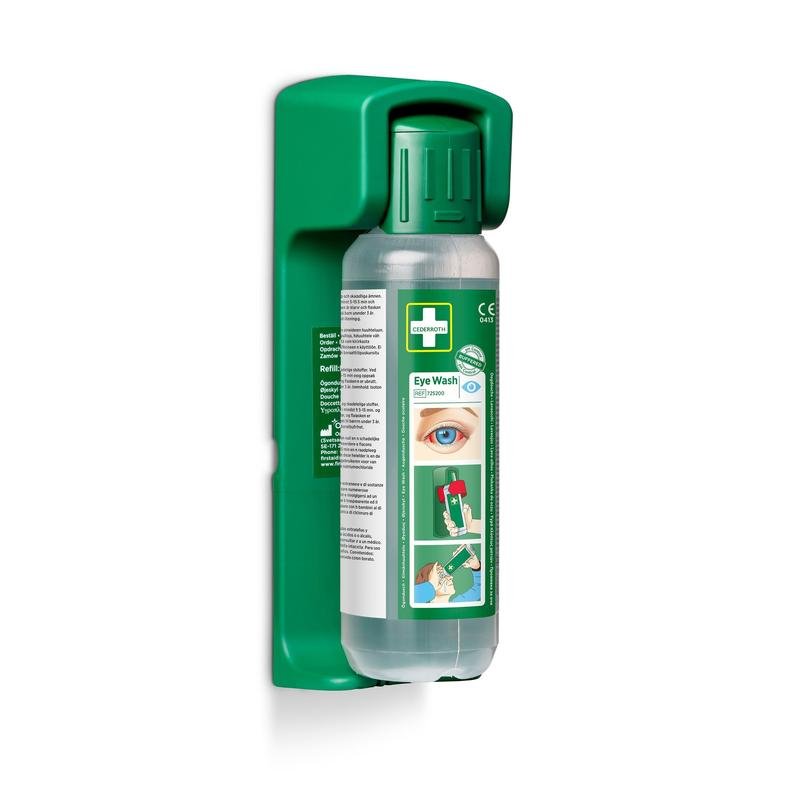 Egy 500 ml-es szemöblítő palack az Orkla Wound Care AB-től egy falra szerelhető tartóban van elhelyezve (500 ml-es szemöblítéshez); tartalmaz egy foszforeszkáló figyelmeztető táblát. A palack illusztrált utasításokat és egy szemet mutat a címkén.