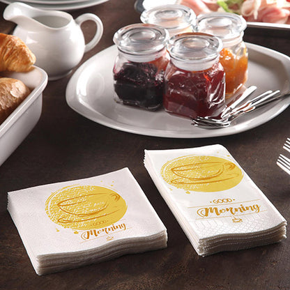 Egy reggelizőasztal croissant-okkal, egy kannával és 200 PAPSTAR szalvétával (3 rétegű 1/4-hajtás, 24x24 cm) a PAPSTAR GmbH-tól, „Jó reggelt” felirattal, valamint lekváros üvegekkel és három villával egy kényelmes reggelihez.