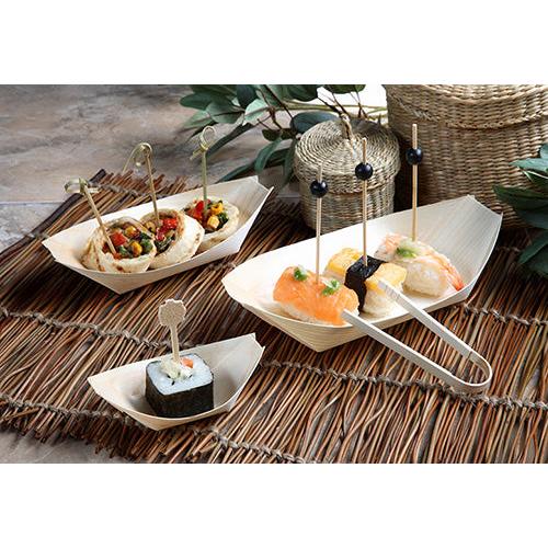 Fingerfood sushi és előételek a PAPSTAR 50 darabos fingerfood fa "pure" csónak tálcáin a PAPSTAR GmbH-tól, minden darab dekoratív pálcikán, bambusz alátéteken zöld levelekkel és fonott kosarakkal a háttérben.