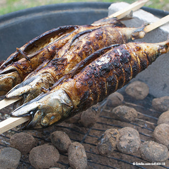 Két egész Steckerlfisch van felnyársalva a PAPSTAR grillnyársakra "pure" 80 cm (20 darab) a PAPSTAR GmbH-tól, és izzó faszén felett grillezve, miközben a bőr az izzó szén felett elszenesedik és ropogós lesz.