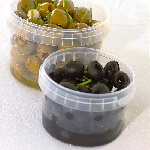 Két átlátszó Starpak 30 finomságos pohárban (770 ml, PP, Ø 11,8 cm · 11,3 cm) eredetiségzárral olívabogyók vannak elhelyezve fehér alapon - a hátsó pohárban zöld olívabogyók fűszerekkel, elöl pedig fekete olívabogyók fűszerdísszel.