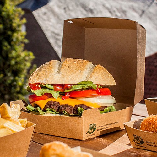Egy sajtburger salátával, paradicsommal, hagymával és cheddar sajttal a szabadban fekszik egy PAPSTAR GmbH kartonból készült hamburgerdoboz (9x18,5x18,5 cm, „100% Fair”, 25 darab). A sült krumplit és az egyéb köreteket külön, mellé tálalják.