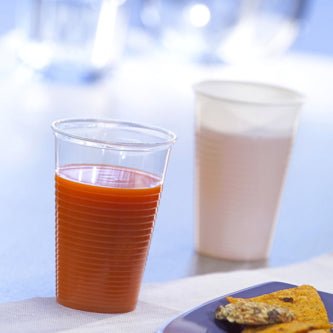 Egy narancslével töltött Starpak 25 ivópohár (PP, 0,2 l, Ø 7,03 cm × 9,9 cm) mellett egy könnyű itallal teli fehér műanyag pohár áll, előtte egy ételtányér részlete látható – tökéletes útközbeni élvezethez.