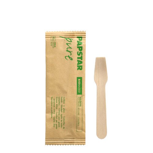 Egy PAPSTAR fagylaltkanál fa "pure" 9,4 cm, egyenként papírba csomagolva zöld "PAPSTAR pure BIO-BASED" felirattal, egy PAPSTAR GmbH barna csomagolása mellett fehér háttéren fekszik.