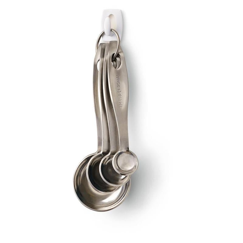 Négy rozsdamentes acél mérőkanál egy fémgyűrűn lóg egy 3M Deutschland GmbH Command™ Mini-Hook, 17006 kampón - biztonságosan rögzítve fúrás nélkül, és könnyen, nyom nélkül eltávolítható a fehér falról.