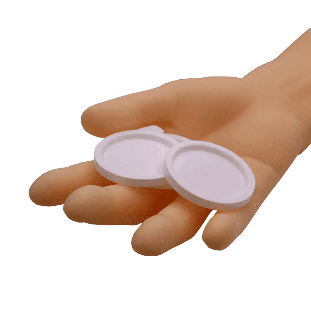 Egy kéz két kerek AMPri fedelet tart gyógyszeres poharakhoz, fehér tárgyak egyszerű fehér háttér előtt.