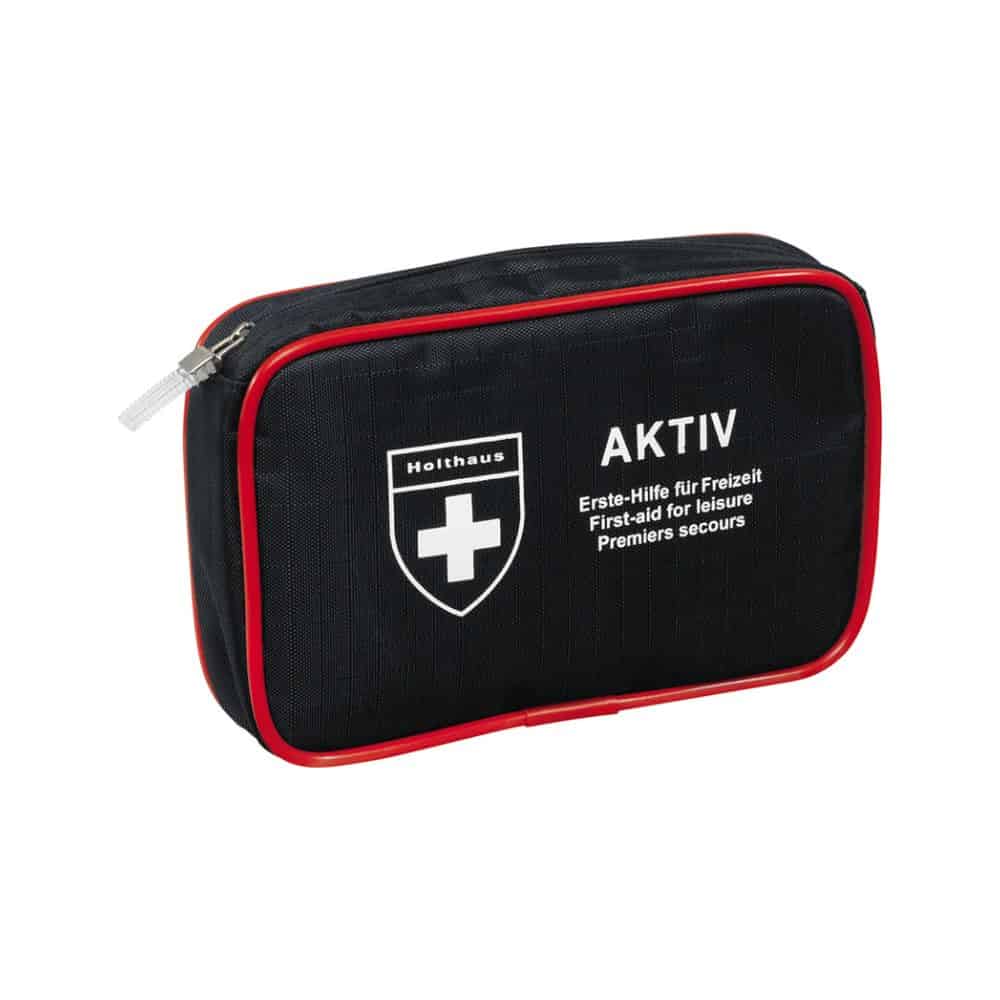 Egy kompakt fekete elsősegély-készlet piros szegéllyel és cipzárral, fehér keresztlogóval és a „Holthaus Medical AKTIV” valamint „Erste-Hilfe für Freizeit / First-aid for Leisure / Premiers secours” szövegekkel az elején. Tökéletes útközben és otthonra.