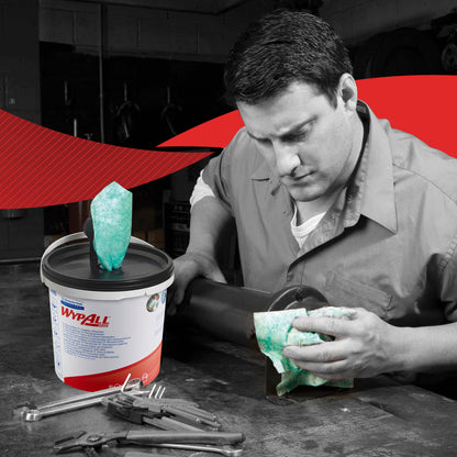 Ein Mann in Arbeitskleidung reinigt ein Metallrohr mit einem grünen WypAll® Wischtuch von Kimberly-Clark GmbH. Ein Karton (6 Spendereimer) der Tücher liegt zwischen Werkzeugen. Das Foto ist größtenteils schwarz-weiß, abgesehen von den Tüchern und dem Etikett.