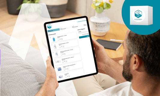 Ein Mann sitzt auf einer Couch und hält ein Tablet in der Hand, auf dem eine Schnittstelle für die Bestellung von medizinischen Rezepten oder Produkten angezeigt wird. In der oberen rechten Ecke ist ein Kasten mit einem blauen Logo und dem Wort "ALTERNAMEDIX" zu sehen.