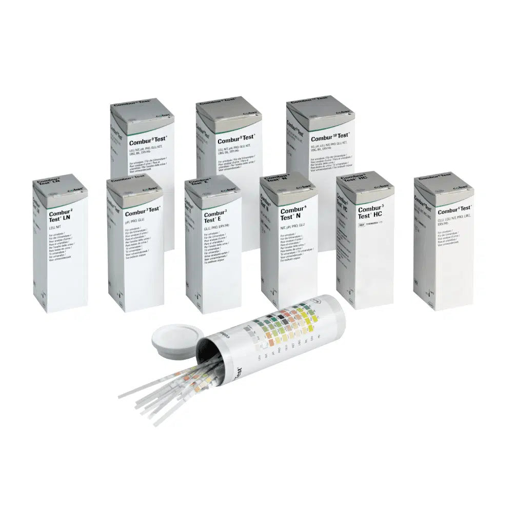 Hinter einem offenen zylindrischen Behälter mit Deckel verbergen sich neun Schachteln mit der Aufschrift „Combur®“ der Servoprax GmbH, die jeweils 100 Roche Urinteststreifen enthalten. An der Seite des Behälters ist eine mehrfarbige Tabelle angebracht, die sich perfekt für die Durchführung eines Schnelltests eignet.