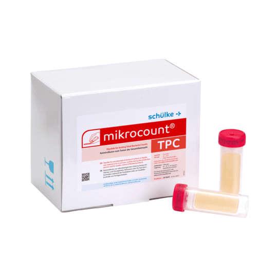 Egy fehér doboz, amelyen a „Schülke & Mayr GmbH Mikrocount® TPC, táptalaj | csomag (20 darab)” felirat, egy logó és a termékleírás látható, mellette két mikrobiológiai vizsgálatra szolgáló fiolával: az egyik sárga fedéllel, a másik átlátszó fedéllel.