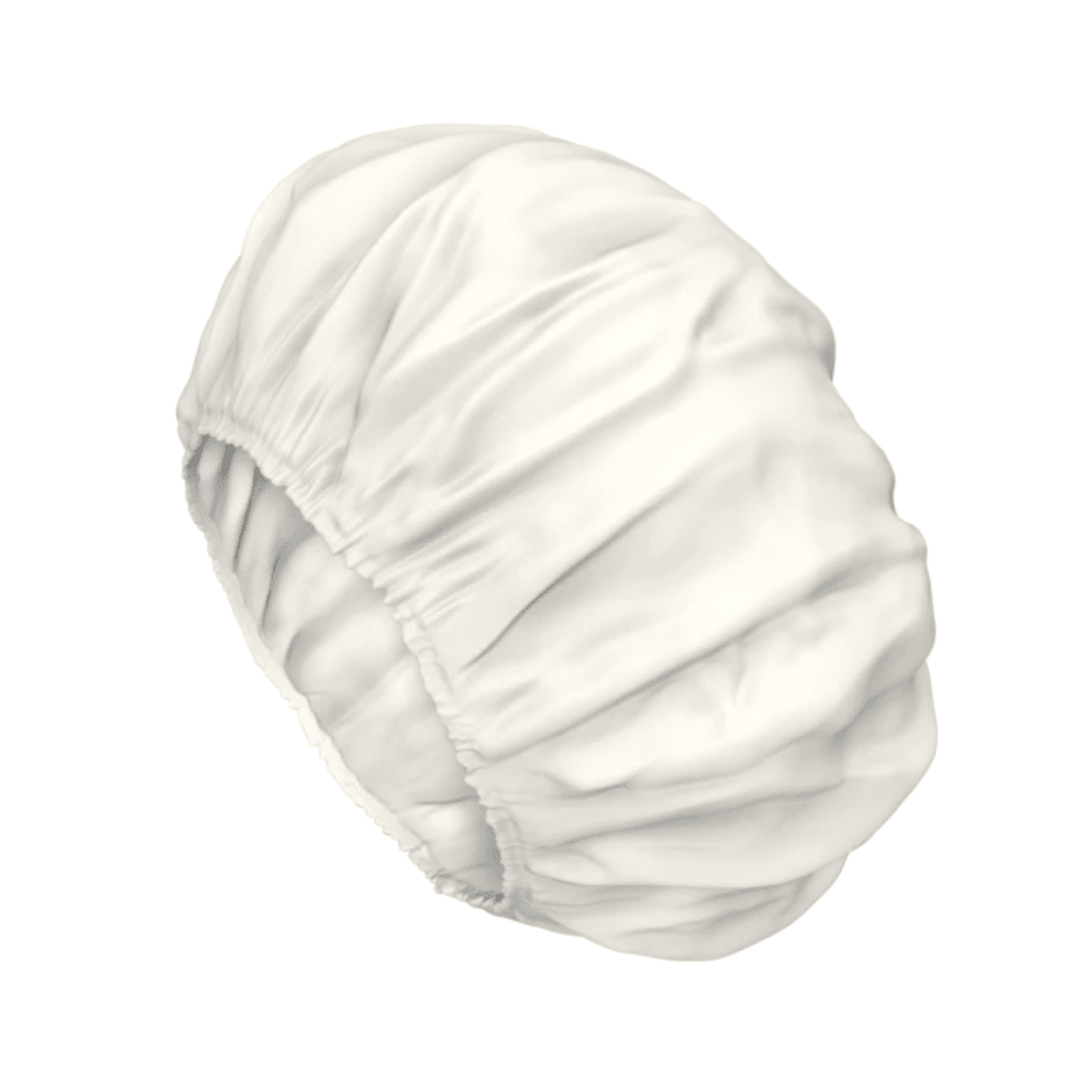 Egy fehér szatén sapka ráncolt, rugalmas szélekkel a haj védelmére, amely a TENA ProSkin Shampoo Cap mosósapka gyengéd ápolására emlékeztet.