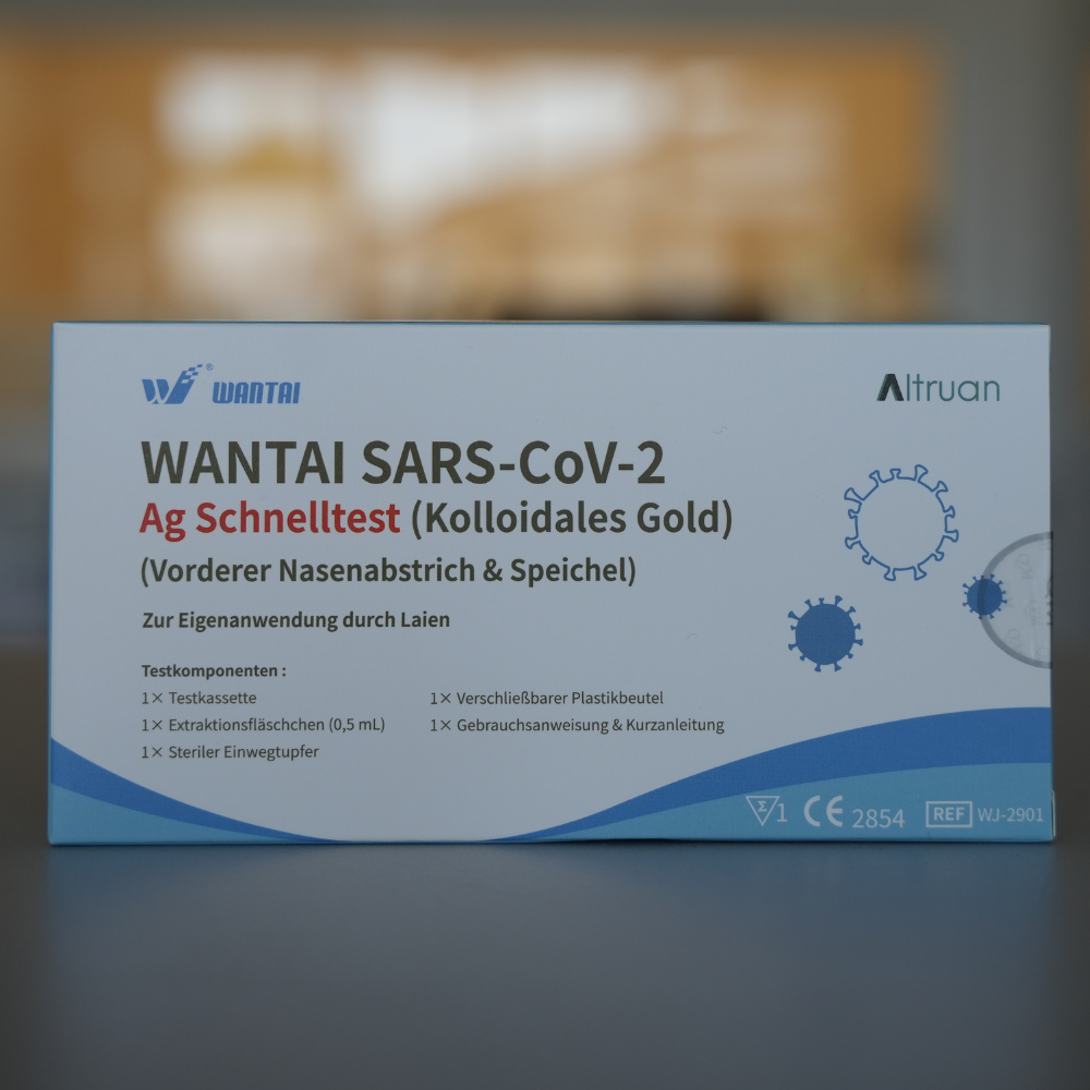 Eine Schachtel Wantai SARS-Cov-2 Schnelltest, Lollitest (Kollodiales Gold) CE/2854 wird ausgestellt. Die Verpackung ist blau und weiß mit einem Diagramm des Virus und einem deutschen Text, der den Test für Nasen- und Speichelproben beschreibt. Die Logos CE und Altruan sind deutlich zu erkennen.