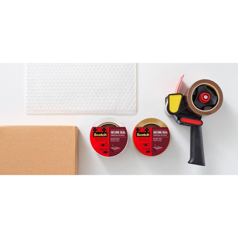 Egy tekercs buborékfólia, egy kartondoboz, két tekercs 3M Deutschland GmbH Scotch® csomagolószalag (50 mm x 66 m) és egy fekete szalagadagoló egy fehér felületen van elrendezve.