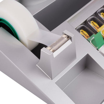 Közelkép a 3M Deutschland GmbH Post-it® asztali rendezőjéről, amely Post-it® jegyzetlapokat, indexeket és Scotch® Magic™ ragasztószalagot (1 darab) tartalmaz, bemutatva a fogazott élű ragasztószalag-adagolót és a szomszédos asztali rendező rekeszeket.