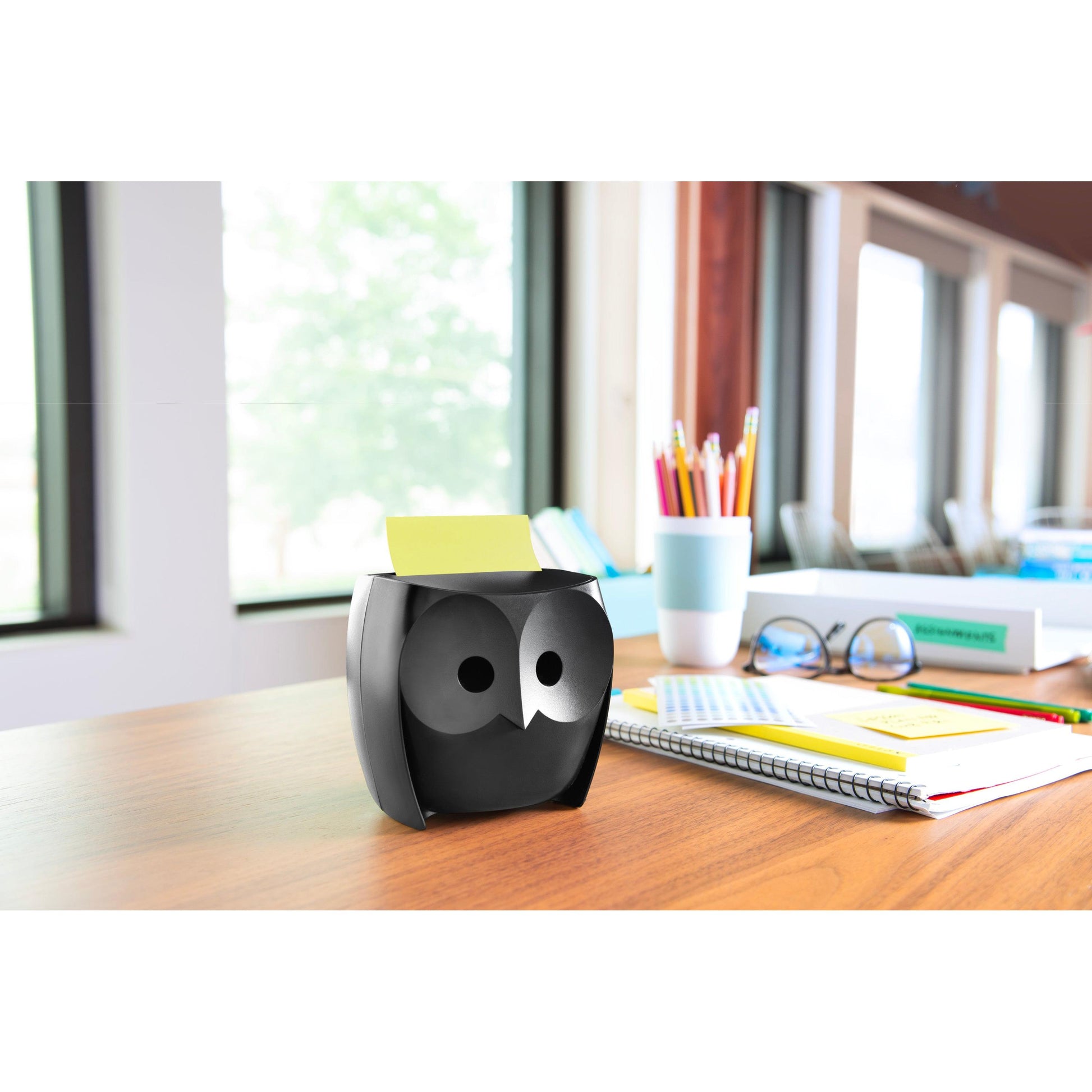 Ein Post-it® Z-Notes Dispenser in schwarzer Eulenform (Eule, Schwarz) von 3M Deutschland GmbH steht auf einem Schreibtisch mit Buntstiften, Notizbüchern, einer blauen Tasse und Super Sticky Z-Notes (45 Blatt/Block, 2 Blöcke/Packung) - ein charmantes Accessoire.